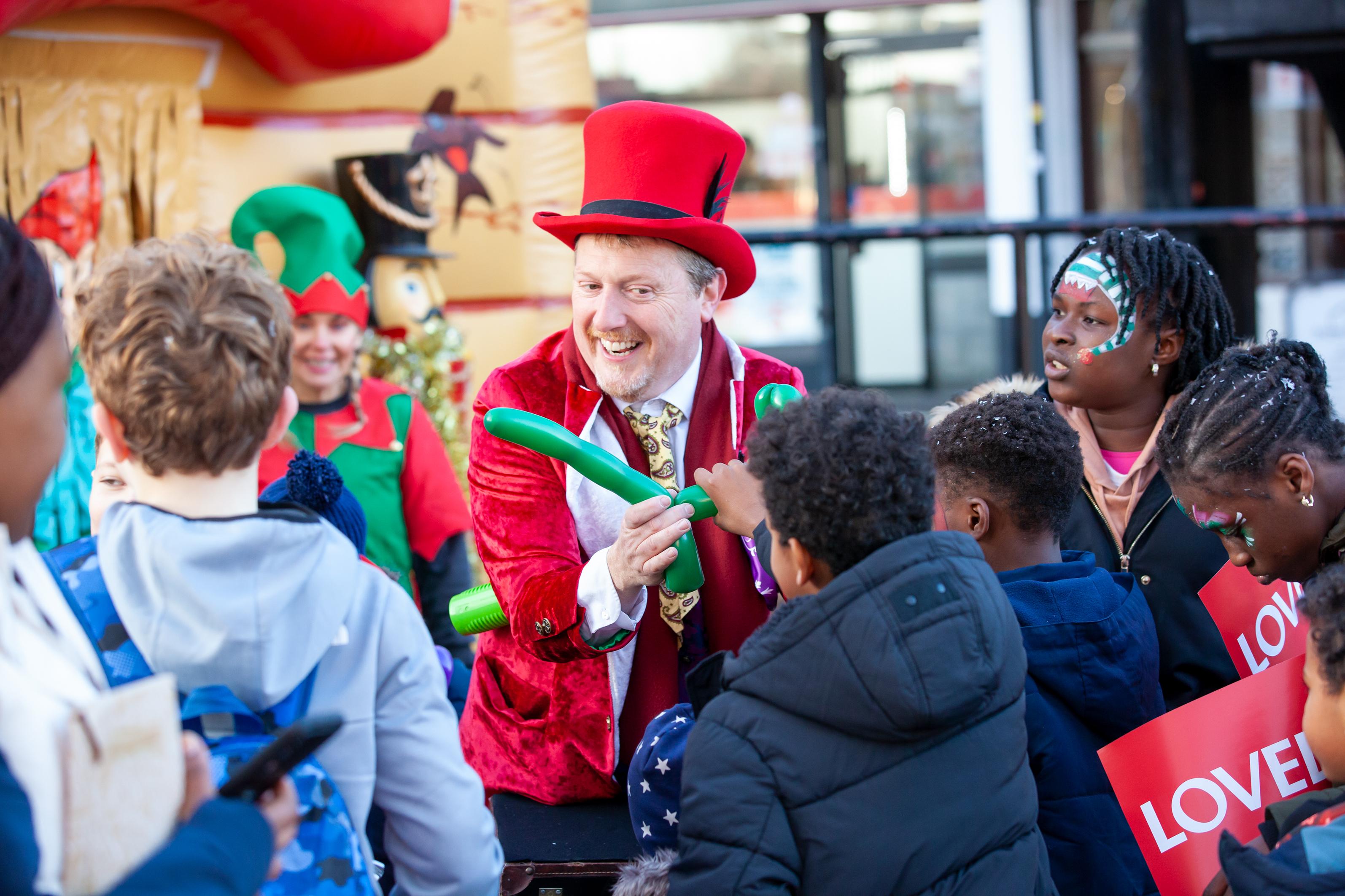 Person in top hat making a balloon animal in front of children