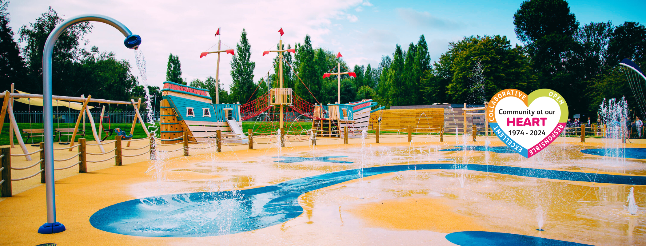 splashpark with sprinklers and play equipment including a pirate ship and the community at our heart logo